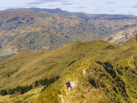 Aerial view of a hiker walking along the grassy ridge of the Quilotoa caldera with rugged mountain slopes and a clear sky in Quilotoa Cotopaxi Ecuador. Aerial view of a hiker walking along the grassy ridge of the Quilotoa caldera with rugged mountain slopes and a clear sky in Quilotoa Cotopaxi Ecuador.