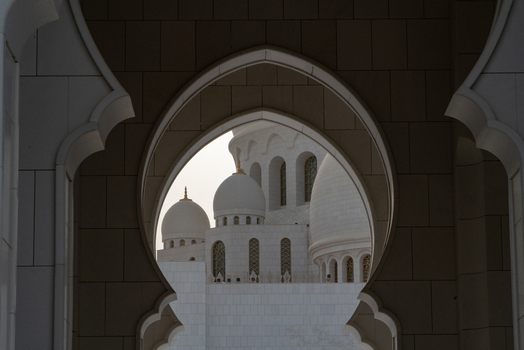 View of the white marble domes and intricate Islamic arches of a grand mosque framed by a stone archway in Abu Dhabi Abu Dhabi United Arab Emirates. View of the white marble domes and intricate Islamic arches of a grand mosque framed by a stone archway in Abu Dhabi Abu Dhabi United Arab Emirates.