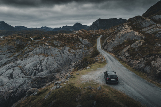 View of a black car parked on a winding road through the rugged rocky landscape of Nesland in Flakstad Municipality Nordland Norway. View of a black car parked on a winding road through the rugged rocky landscape of Nesland in Flakstad Municipality Nordland Norway.