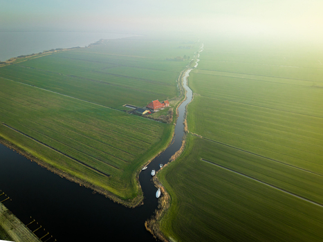 Aerial view of a narrow canal winding through green polders with a farmhouse and small boats Sloten Friesland Netherlands. Aerial view of a narrow canal winding through green polders with a farmhouse and small boats Sloten Friesland Netherlands.