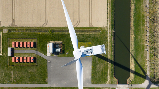 Aerial view of a large white wind turbine casting a long shadow over a canal and utility buildings in Middelharnis South Holland Netherlands. Aerial view of a large white wind turbine casting a long shadow over a canal and utility buildings in Middelharnis South Holland Netherlands.