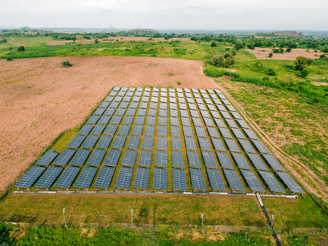 Aerial view of a large solar farm with rows of photovoltaic panels installed in a rural landscape with green fields and distant hills in Ogun State Nigeria.