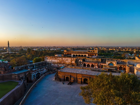 Aerial view of Lahore Fort featuring historic Mughal architecture expansive courtyards and surrounding city skyline under a clear golden hour sky in Lahore Punjab Pakistan.