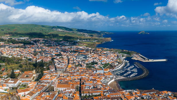Aerial view of the historic city center with red roofed houses and the harbor along the blue coastline Angra do Heroismo Azores Portugal.