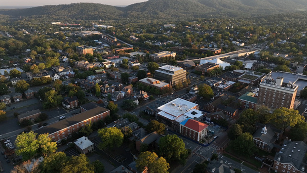 Aerial view of the city of Charlottesville featuring urban architecture residential areas and lush green trees nestled against rolling hills in Charlottesville Virginia United States.