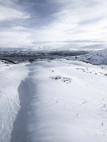 Aerial view of snow covered mountain ridges overlooking a fjord under a cloudy winter sky in Kvaloya Troms Norway. Aerial view of snow covered mountain ridges overlooking a fjord under a cloudy winter sky in Kvaloya Troms Norway.