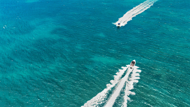 Aerial view of two speedboats cruising across vibrant turquoise tropical waters leaving long white wakes behind them in the Indian Ocean Beau Vallon Beau Vallon Seychelles.