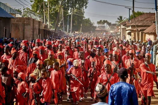 Zaria City Nigeria 21 March 2026 View of a vibrant crimson procession a sea of red garments and traditional weapons filling a dusty street with cultural fervor. Zaria City Nigeria 21 March 2026 View of a vibrant crimson procession a sea of red garments and traditional weapons filling a dusty street with cultural fervor.