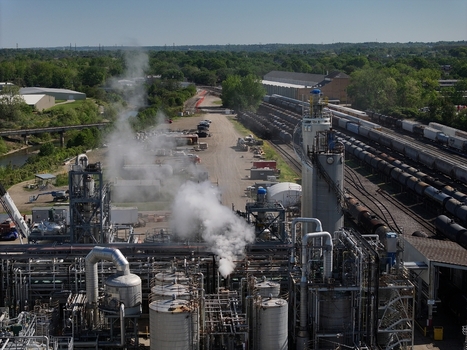 Aerial view of an industrial chemical plant featuring storage tanks complex piping with rising steam and freight trains on adjacent tracks in Cincinnati OH United States. Aerial view of an industrial chemical plant featuring storage tanks complex piping with rising steam and freight trains on adjacent tracks in Cincinnati OH United States.