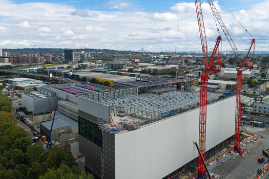 Aerial view of a large data center under construction with red cranes steel framework and surrounding urban landscape in the United Kingdom.