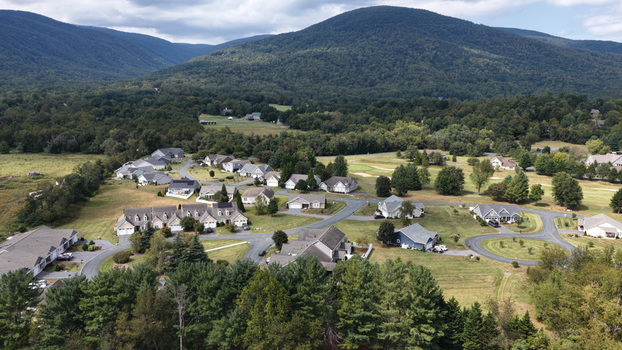 Aerial view of a residential neighborhood with houses winding roads and lush green lawns nestled against a backdrop of rolling mountains in Nellysford Virginia United States. Aerial view of a residential neighborhood with houses winding roads and lush green lawns nestled against a backdrop of rolling mountains in Nellysford Virginia United States.