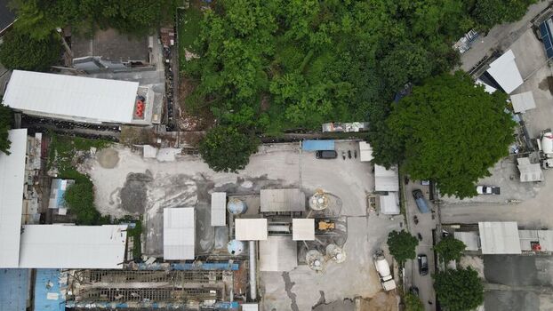 Aerial view of a concrete batching plant with industrial silos and mixer trucks surrounded by lush trees in Kecamatan Menteng Daerah Khusus Ibukota Indonesia. Aerial view of a concrete batching plant with industrial silos and mixer trucks surrounded by lush trees in Kecamatan Menteng Daerah Khusus Ibukota Indonesia.