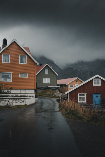 View of traditional wooden houses in the coastal village of Henningsvaer under a dramatic cloudy sky with mountains in the background Henningsvaer Nordland Norway. View of traditional wooden houses in the coastal village of Henningsvaer under a dramatic cloudy sky with mountains in the background Henningsvaer Nordland Norway.