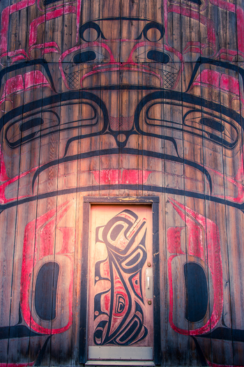 View of the intricately carved wooden totem pole and longhouse entrance featuring traditional indigenous art at Ksan British Columbia Canada. View of the intricately carved wooden totem pole and longhouse entrance featuring traditional indigenous art at Ksan British Columbia Canada.