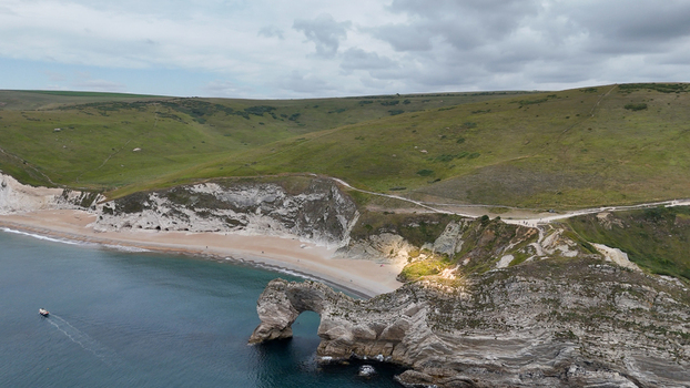 Aerial view of Durdle Door a natural limestone arch on the Jurassic Coast featuring rugged cliffs a sandy beach and calm blue sea in Wareham England United Kingdom. Aerial view of Durdle Door a natural limestone arch on the Jurassic Coast featuring rugged cliffs a sandy beach and calm blue sea in Wareham England United Kingdom.