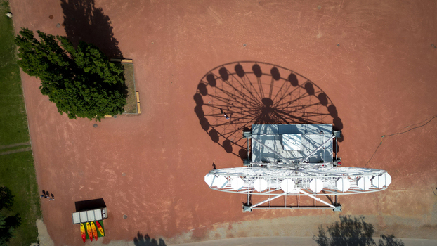 Aerial view of a carousel casting a geometric shadow on the reddish brown ground near verdant trees creating a striking contrast of shapes and colors Neuchâtel Neuchâtel Switzerland. Aerial view of a carousel casting a geometric shadow on the reddish brown ground near verdant trees creating a striking contrast of shapes and colors Neuchâtel Neuchâtel Switzerland.