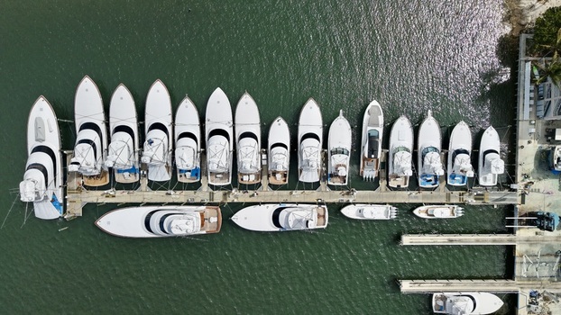 Aerial view of numerous white yachts and luxury boats moored at a wooden pier with people walking along the dock at Peanut Island in Palm Beach County Florida United States.