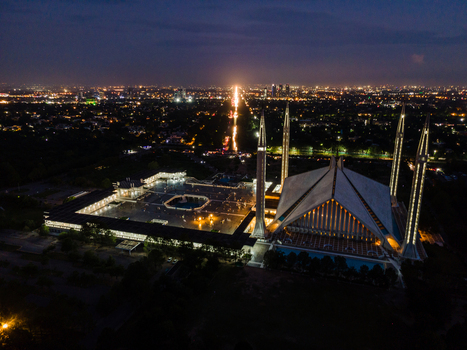 Aerial view of the illuminated Faisal Masjid with its iconic tent shaped architecture and four tall minarets against the glowing city skyline at night in Islamabad Islamabad Capital Ter Pakistan. Aerial view of the illuminated Faisal Masjid with its iconic tent shaped architecture and four tall minarets against the glowing city skyline at night in Islamabad Islamabad Capital Ter Pakistan.
