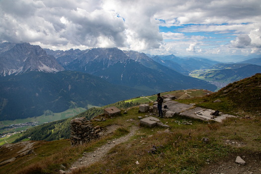 View of the Dolomites mountain range with stone ruins and a person standing on a grassy ridge under a cloudy sky in Rocca Pietore Veneto Italy. View of the Dolomites mountain range with stone ruins and a person standing on a grassy ridge under a cloudy sky in Rocca Pietore Veneto Italy.