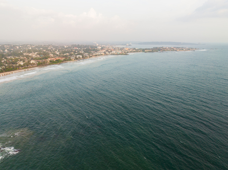 Aerial view of the coastline featuring urban buildings tropical trees and ocean waves under a hazy sky in Galle Southern Province Sri Lanka.