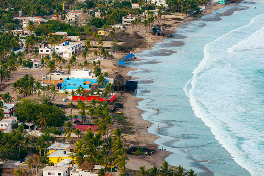 Aerial view of Punta Perula beach with colorful houses palm trees and waves crashing on the sandy shore in Punta Perula Jalisco Mexico. Aerial view of Punta Perula beach with colorful houses palm trees and waves crashing on the sandy shore in Punta Perula Jalisco Mexico.