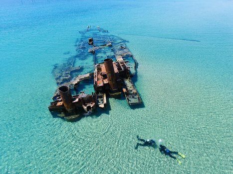 Aerial view of the Shipwreck Epanomi with its rusty hull submerged in crystal clear turquoise water and two divers swimming nearby Epanomi Greece.