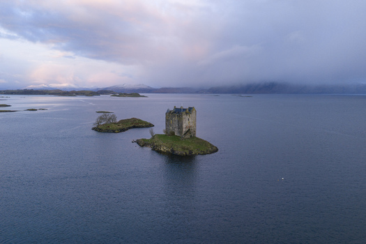 Aerial view of Castle Stalker on a small island in Loch Laich with snow capped mountains and soft twilight clouds Appin Scotland United Kingdom. Aerial view of Castle Stalker on a small island in Loch Laich with snow capped mountains and soft twilight clouds Appin Scotland United Kingdom.