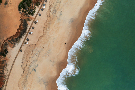 Aerial view of the sandy beach with turquoise ocean waves wooden walkway and parasols along the coastline in Faro Faro District Portugal.