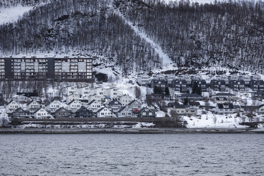 View of modern residential houses and apartment buildings on a snowy hillside overlooking the water in Tromso Troms Norway.