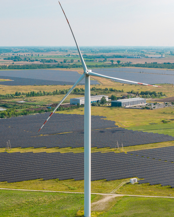 Aerial view of a large wind turbine standing in front of an extensive solar farm with rows of photovoltaic panels in a rural landscape in Konin Greater Poland Voivod Poland. Aerial view of a large wind turbine standing in front of an extensive solar farm with rows of photovoltaic panels in a rural landscape in Konin Greater Poland Voivod Poland.