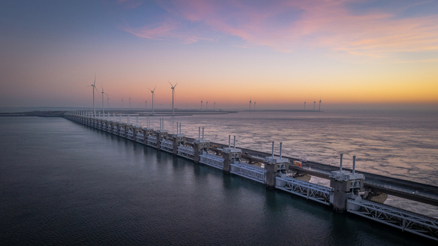 Aerial view of the Oosterscheldekering storm surge barrier and offshore wind turbines under a vibrant sunset sky in Vrouwenpolder Zeeland Netherlands.