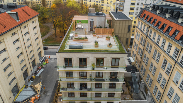 Aerial view of a modern residential building featuring a green roof terrace with wooden decking planters and glass railings situated in an urban neighborhood in Sweden. Aerial view of a modern residential building featuring a green roof terrace with wooden decking planters and glass railings situated in an urban neighborhood in Sweden.