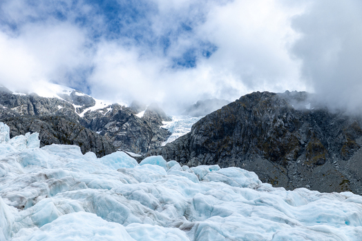 View of glacial ice formations under a cloudy sky with snow capped mountains in the background a scene of cold beauty Franz Josef Glacier West Coast Region New Zealand. View of glacial ice formations under a cloudy sky with snow capped mountains in the background a scene of cold beauty Franz Josef Glacier West Coast Region New Zealand.