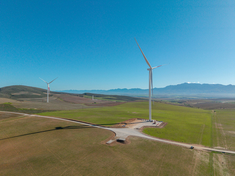 Aerial view of wind turbines standing in green fields with rolling hills and mountains under a clear blue sky in Swellendam Western Cape South Africa. Aerial view of wind turbines standing in green fields with rolling hills and mountains under a clear blue sky in Swellendam Western Cape South Africa.