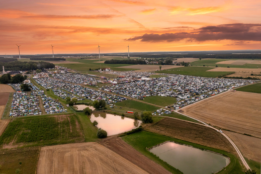Aerial view of the Open Beatz Festival campsite with thousands of tents small ponds and wind turbines under a golden sunset sky in Herzogenaurach Bayern Germany. Aerial view of the Open Beatz Festival campsite with thousands of tents small ponds and wind turbines under a golden sunset sky in Herzogenaurach Bayern Germany.