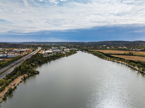 Aerial view of Lake Torokbalint beside the M1 highway with traffic industrial buildings farmland and wooded hills in Biatorbagy Hungary under clouds. Aerial view of Lake Torokbalint beside the M1 highway with traffic industrial buildings farmland and wooded hills in Biatorbagy Hungary under clouds.