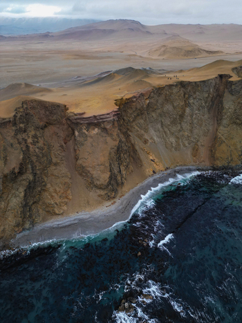 Aerial view of Reserva Nacional de Paracas with steep coastal cliffs a narrow shoreline and vast desert plains under a cloudy sky Paracas Ica Peru.