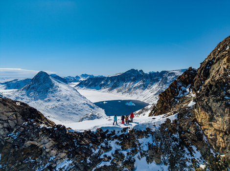 Aerial view of people standing on a snowy mountain ridge overlooking a deep blue fjord with icebergs and rugged peaks under a clear sky Tasiilaq Sermersooq Municipali Greenland. Aerial view of people standing on a snowy mountain ridge overlooking a deep blue fjord with icebergs and rugged peaks under a clear sky Tasiilaq Sermersooq Municipali Greenland.