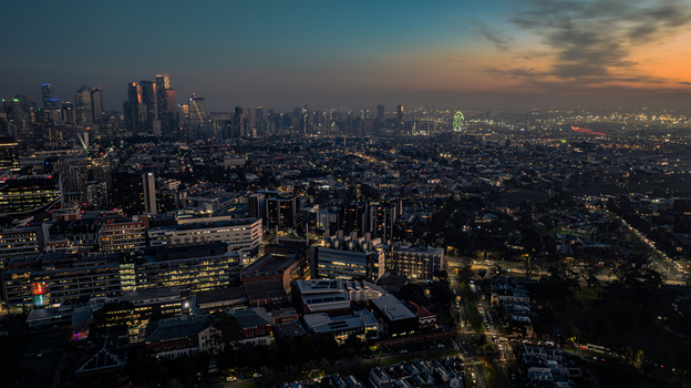 Aerial view of the Melbourne skyline at twilight featuring illuminated skyscrapers residential areas and a distant Ferris wheel in Parkville Victoria Australia. Aerial view of the Melbourne skyline at twilight featuring illuminated skyscrapers residential areas and a distant Ferris wheel in Parkville Victoria Australia.