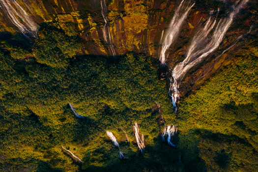 Aerial view of Poco da Ribeira do Ferreiro waterfalls cascading down a steep mossy cliff into lush vegetation during golden hour Fajazinha Azores Portugal. Aerial view of Poco da Ribeira do Ferreiro waterfalls cascading down a steep mossy cliff into lush vegetation during golden hour Fajazinha Azores Portugal.