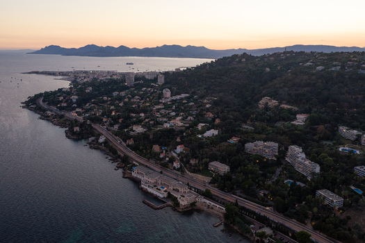 Aerial view of the coastline at sunset featuring coastal roads residential buildings nestled in lush greenery and the Mediterranean Sea in Antibes Provence Alpes Cote d Azur France. Aerial view of the coastline at sunset featuring coastal roads residential buildings nestled in lush greenery and the Mediterranean Sea in Antibes Provence Alpes Cote d Azur France.