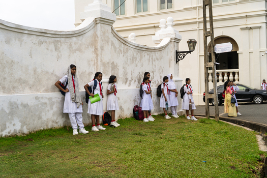 Sri Lanka 07 January 2026 View of schoolgirls in white uniforms standing by a weathered white wall outside a historic colonial building.