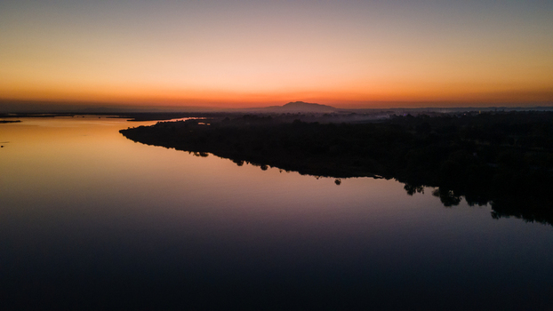 Aerial view of the Jhelum River at sunset with the silhouette of hills and the city skyline under a glowing orange sky in Jhelum Punjab Pakistan. Aerial view of the Jhelum River at sunset with the silhouette of hills and the city skyline under a glowing orange sky in Jhelum Punjab Pakistan.