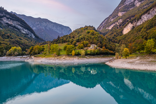 Aerial view of Lago di Tenno with its turquoise waters reflecting the surrounding autumn mountains and a small house on the shore in Tenno Trentino Alto Adige Italy.