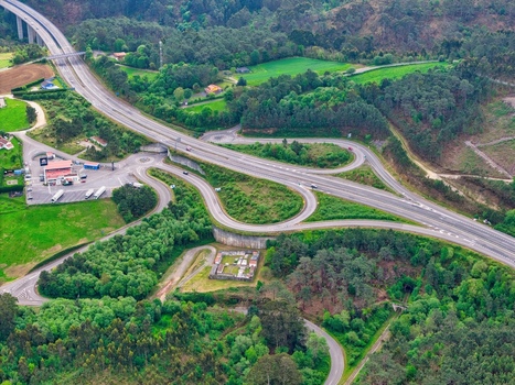 Aerial view of a highway interchange with winding roads and a bridge surrounded by lush green forests and hills in Cudillero Asturias Spain.