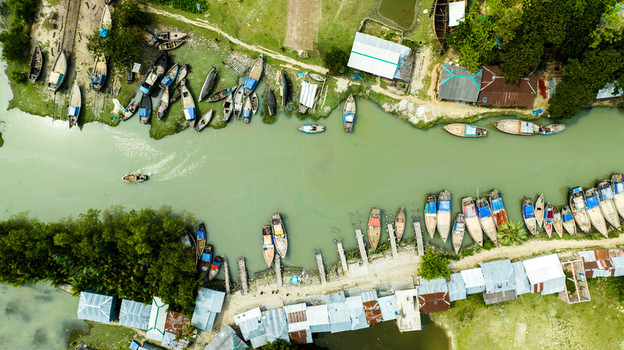 Aerial view of numerous wooden boats moored along the riverbank near small buildings with metal roofs in Patharghata Barisal Division Bangladesh. Aerial view of numerous wooden boats moored along the riverbank near small buildings with metal roofs in Patharghata Barisal Division Bangladesh.