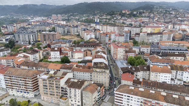 Aerial view of the urban landscape with dense residential buildings red tiled rooftops and misty green hills under an overcast sky in Ourense Province of Ourense Spain.