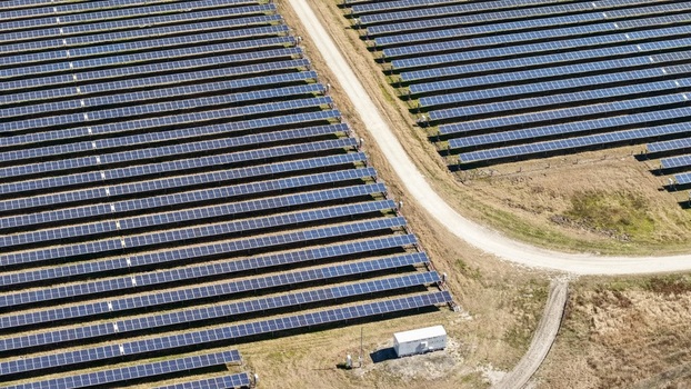 Aerial view of rows of solar panels stretching across the landscape bisected by a winding dirt road under the bright sky Elkton Florida United States. Aerial view of rows of solar panels stretching across the landscape bisected by a winding dirt road under the bright sky Elkton Florida United States.