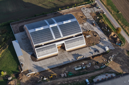 Aerial view of a modern building with extensive solar panels on its roof situated in a construction site with heavy machinery and paved surroundings in Uckermark Brandenburg Germany. Aerial view of a modern building with extensive solar panels on its roof situated in a construction site with heavy machinery and paved surroundings in Uckermark Brandenburg Germany.