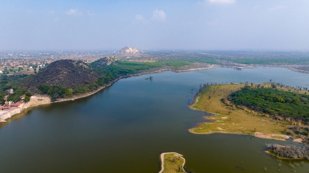 Aerial view of a serene reservoir surrounded by arid hills and sparse vegetation in the landscape near Jodhpur Rajasthan India. Aerial view of a serene reservoir surrounded by arid hills and sparse vegetation in the landscape near Jodhpur Rajasthan India.